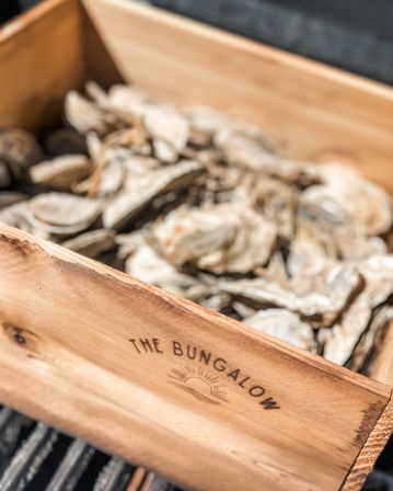 Close-up of a rustic wooden box filled with shucked oyster shells resting on a grill