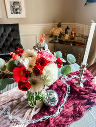 Vibrant red, pink and white flower bouquet with disco-ball ornaments and tiny flamingo toppers on a burgundy velvet runner as a dining table centerpiece