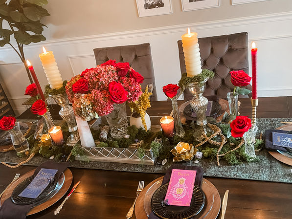 Elegant indoor dining room table centerpiece with red roses and pink hydrangeas, tall twisted and taper candles, moss and gold accents, layered black and copper place settings and purple menu cards for a cozy romantic dinner