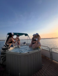Friends in swimsuits on a pontoon boat hot tub posing for photos at sunset over a calm coastal bay