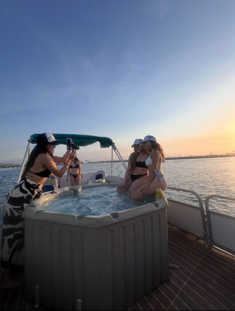 Friends in swimsuits on a pontoon boat hot tub posing for photos at sunset over a calm coastal bay