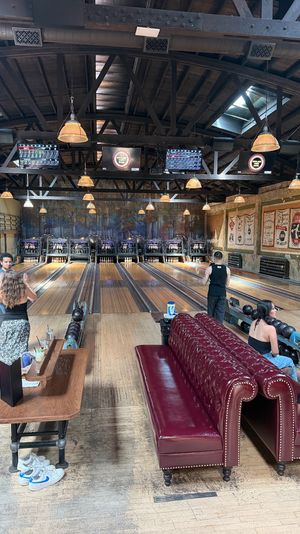 Vintage bowling alley interior with wooden lanes, exposed dark-beam ceiling, hanging pendant lights, tufted red leather sofas and bowlers.