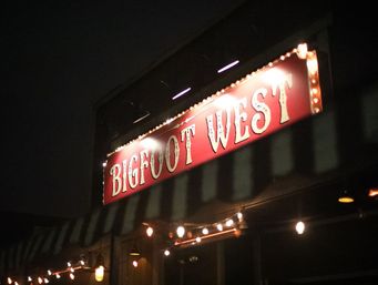 Nighttime storefront with a glowing red vintage marquee sign, twinkling string lights along a striped awning, and warm exterior bulbs.