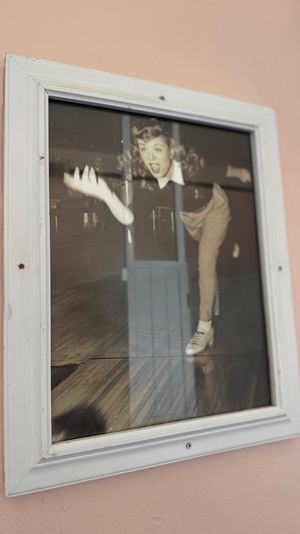 Framed vintage bowling photo of a woman mid-throw wearing retro sneakers, set in a white wooden frame mounted on a pastel pink wall