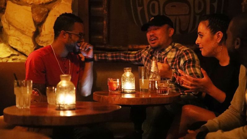 Group of friends laughing and chatting over drinks at a candlelit booth in a cozy urban bar, night out vibes