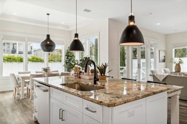 Bright open-concept kitchen with polished granite island, matte-black pendant lights, white cabinetry, dining nook and large windows flooding the space with natural light.