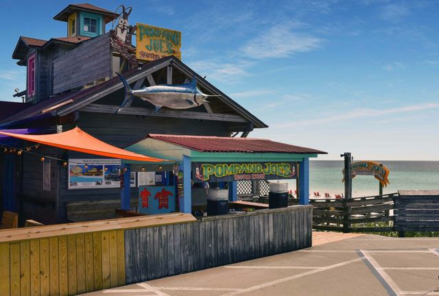 Colorful beachfront seafood shack on a wooden boardwalk with a large mounted marlin, orange canopy, outdoor counter and calm ocean beach in the background