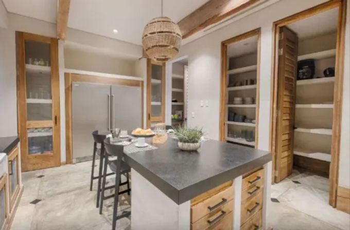Modern farmhouse kitchen with black island countertop and wooden drawers, bar stools, stainless steel double-door fridge, open pantry shelves and a woven pendant light
