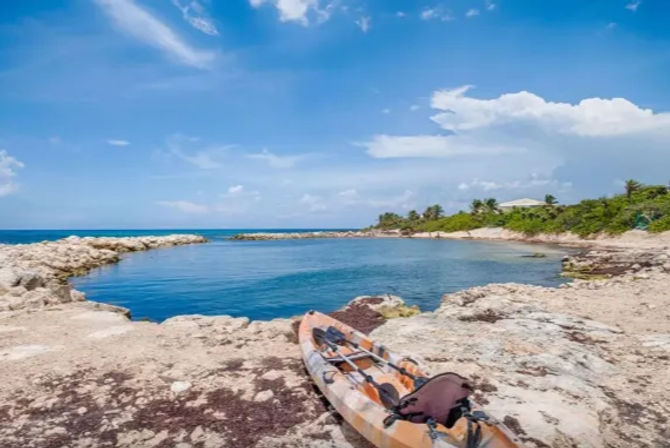 Orange kayak on a rocky shoreline beside a calm turquoise island cove with palm trees under a clear blue sky