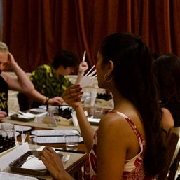 Woman sniffing fragrance strips at an indoor perfume workshop — group scent-sampling class with trays, vials and note cards