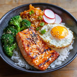 Asian-inspired grilled salmon rice bowl with fluffy white rice, sunny-side-up egg, steamed broccoli, thin radish slices, shredded pickled veggies and sesame seed garnish.