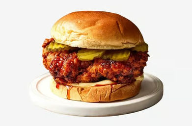 Close-up of a crispy fried chicken sandwich with spicy glaze, pickle slices and mayo on a soft brioche bun, served on a white plate
