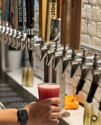 Hand holding a frothy pink craft beer poured from stainless steel draft taps with wooden tap handles on a bar counter