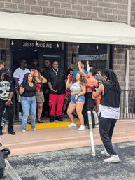 Outdoor party on St. Lucie Ave — a lively group holding red cups dancing and posing outside a storefront while a videographer films.