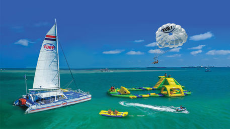 Sunny tropical scene with a white catamaran, colorful inflatable water park, parasail riders, banana boat and jet ski on turquoise sea