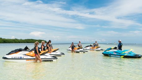 Group of people on colorful jet skis in clear shallow Florida coastal water near mangroves under a sunny blue sky