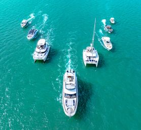Aerial view of white yachts and motorboats cruising turquoise ocean, leisure yachting scene with sunlit water and wake trails.