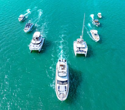 Aerial view of white yachts and motorboats cruising turquoise ocean, leisure yachting scene with sunlit water and wake trails.
