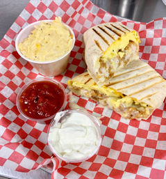 Grilled breakfast wrap halves filled with scrambled eggs, melted cheese and crispy chicken on red checkered paper, served with salsa, sour cream, and a creamy potato side.