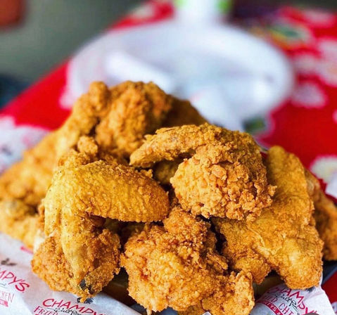 Close-up of a pile of golden, crispy Southern-style fried chicken pieces on a paper-lined plate with creamy dipping sauce blurred in the background.