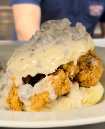 Southern-style crispy fried chicken on a split biscuit smothered in creamy sausage gravy — classic comfort breakfast