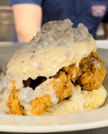 Southern-style crispy fried chicken on a split biscuit smothered in creamy sausage gravy — classic comfort breakfast