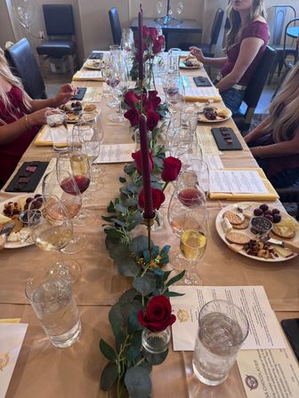 Wine tasting table in an intimate tasting room with rows of wine and champagne glasses, charcuterie plates, red roses and tall burgundy candles.