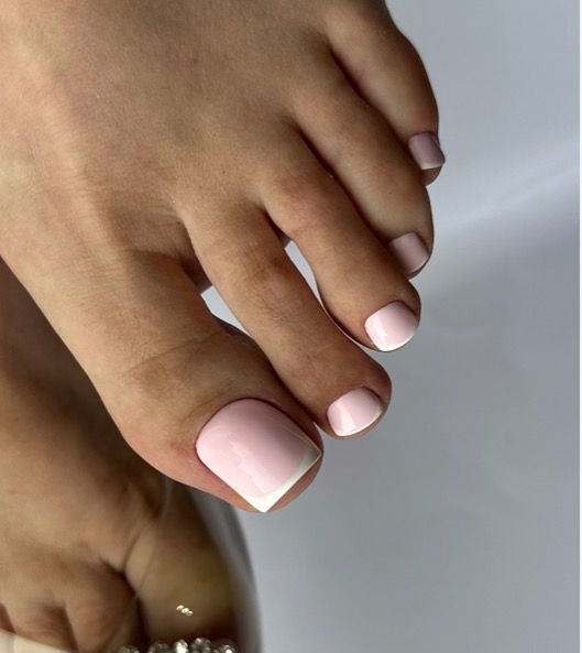 Close-up of toes with a glossy pastel-pink French pedicure on square toenails, neat salon-style finish