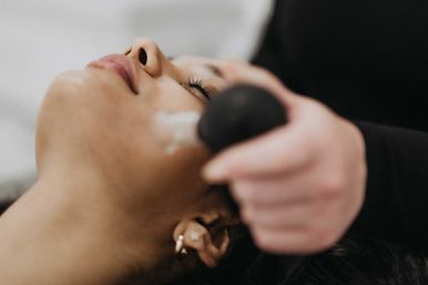 Close-up of a client relaxing during a spa facial while an esthetician applies cream with a round massage tool to the cheek — skincare treatment and pampering.
