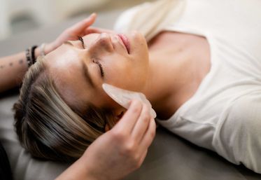 Close-up of a person lying on a spa table receiving a soothing gua sha facial massage with a translucent stone — relaxing skincare treatment.