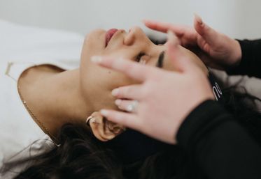 Close-up of a client with eyes closed receiving a relaxing spa facial as an esthetician’s hands gently massage the forehead and temples.