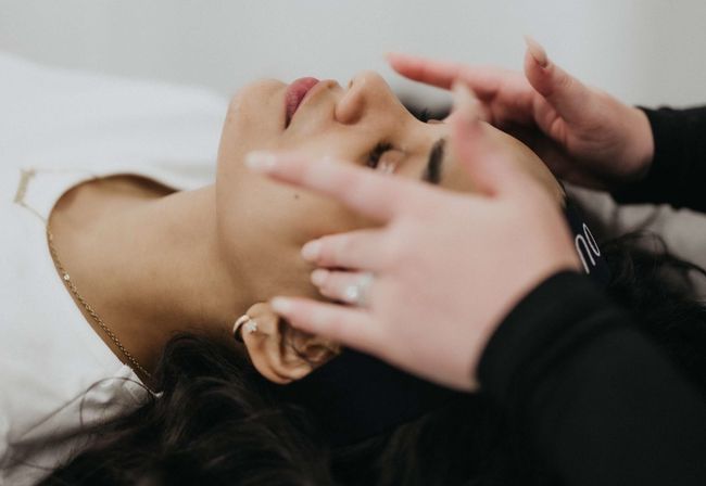 Close-up of a client with eyes closed receiving a relaxing spa facial as an esthetician’s hands gently massage the forehead and temples.