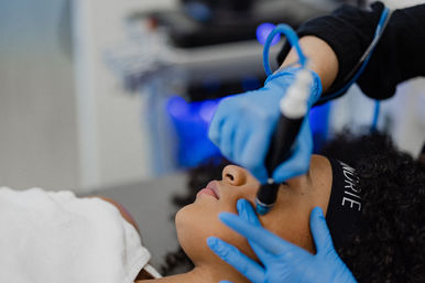 Close-up of a client receiving a professional facial skincare treatment with a handheld device while a technician wearing blue gloves works on the cheek