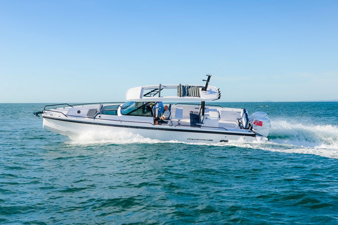 White luxury speedboat with hardtop and outboard engine cutting through turquoise coastal waters, leaving a foamy wake under a bright blue sky