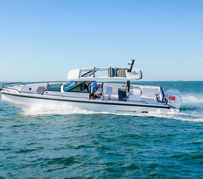 White luxury speedboat with hardtop and outboard engine cutting through turquoise coastal waters, leaving a foamy wake under a bright blue sky
