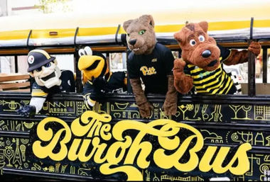 Yellow-and-black decorated bus with four playful sports mascots — a panther, a bee and two costumed characters — leaning from the windows in a festive street scene.