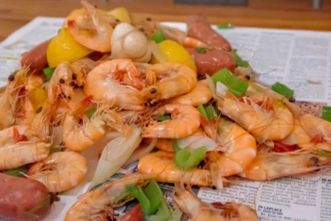 Festive Southern-style shrimp boil: bright orange boiled shrimp piled with sausage, red potatoes, lemon wedges, green bell pepper and onion on newspaper.