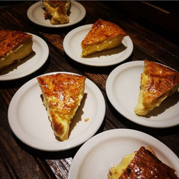 Several slices of creamy custard pie with glossy golden-brown crust served on white plates arranged on a rustic wooden table