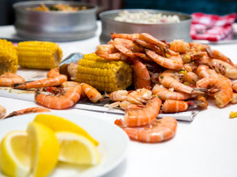 Close-up of a seafood boil: piled cooked shrimp and corn on the cob on a table with lemon wedges and metal serving bowls