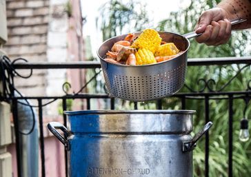 Perforated colander lifting shrimp, potatoes and corn-on-the-cob from a steaming outdoor seafood boil stockpot on a balcony