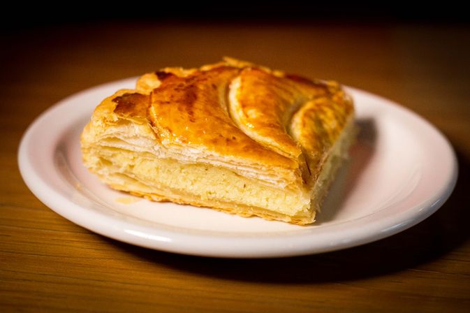 Buttery golden puff pastry square with flaky layers and creamy filling on a white plate set on a wooden table