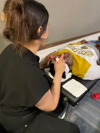 Esthetician applying facial cream to a client lying on a spa table, white towels and skincare supplies nearby — relaxing facial treatment scene.