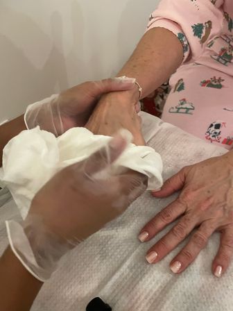 Close-up of a manicure: gloved nail technician wiping a hand with cotton, showing light-pink polished nails and a festive pink sleeve on a salon towel