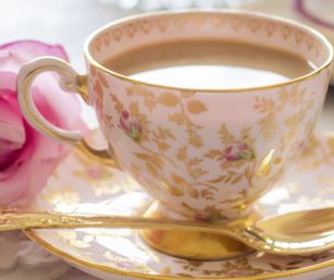 Vintage porcelain teacup with pink rose motifs and gold filigree, filled with tea on a matching saucer with a gold teaspoon