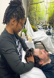 Spa therapist giving a relaxing scalp/head massage to a reclined client in a wellness treatment room with a forest stream mural backdrop