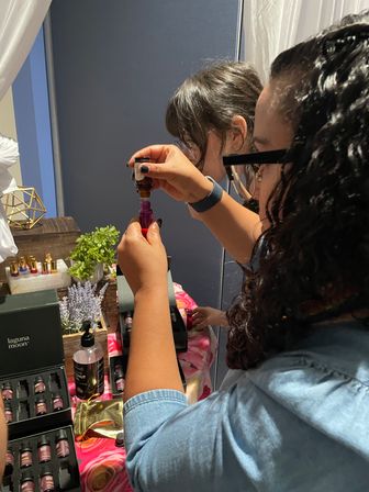 Hands-on aromatherapy: close-up of participants filling a pink roller bottle with essential oil at an indoor workshop table display of small oil bottles, succulents and lavender