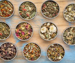Overhead view of colorful loose-leaf herbal tea blends with dried flowers and herbs in round tins arranged on a weathered blue wooden table