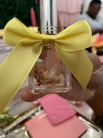 Close-up of a small clear glass bottle with dried flower petals inside, silver cap and bright yellow ribbon bow — hand-held table party favor.