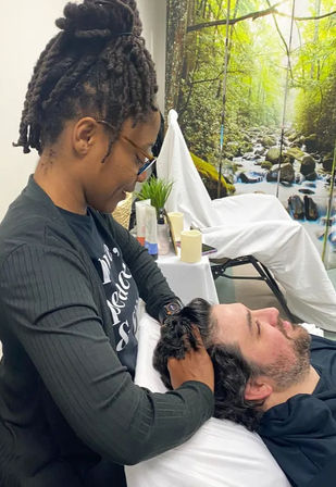 Relaxing head massage in a spa-like treatment room with a forest stream mural, a practitioner massaging a reclining client's scalp.