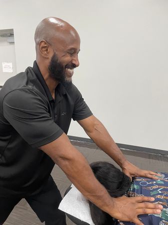 Smiling male massage therapist giving a back adjustment to a client lying face-down on a treatment table in a bright wellness clinic